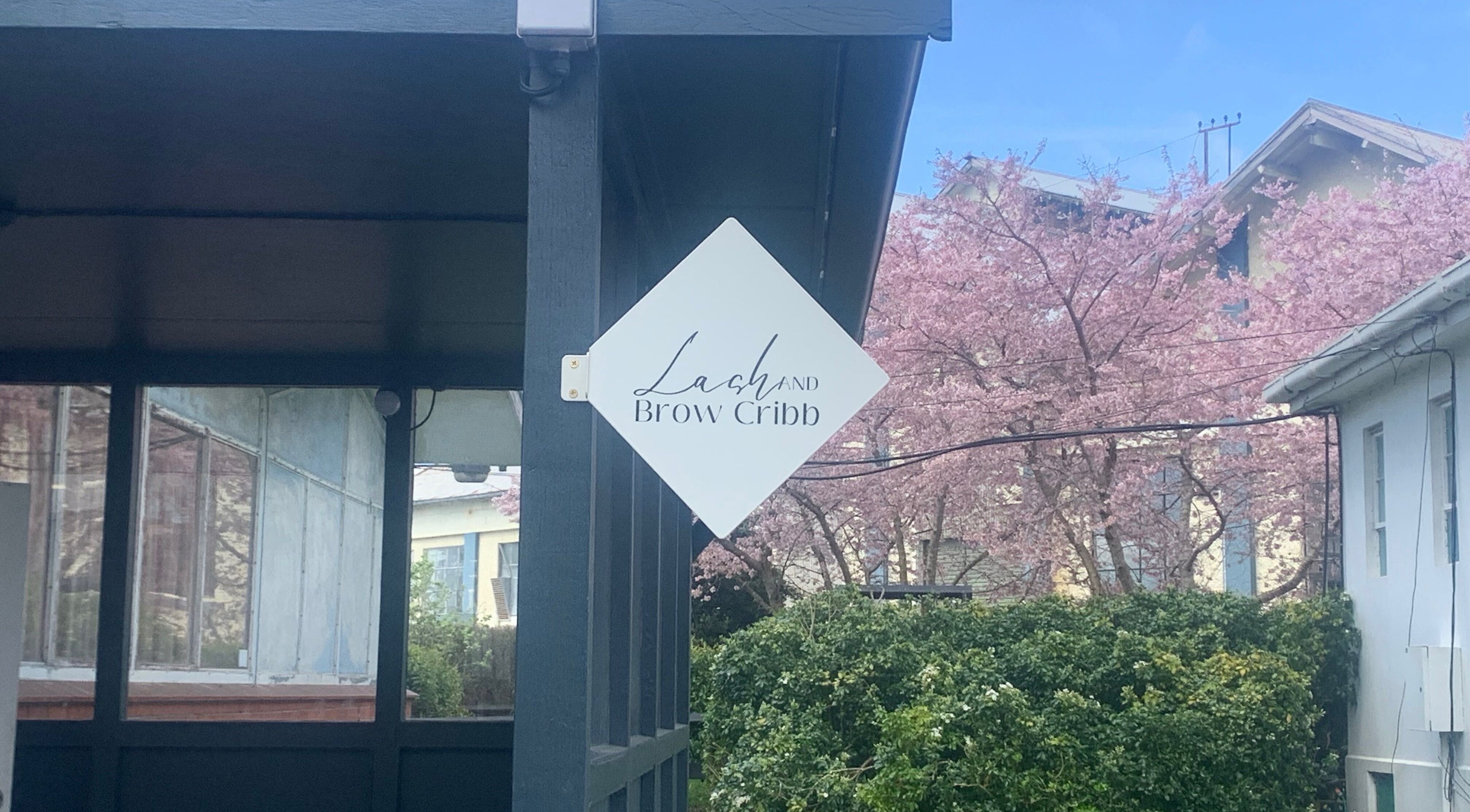 Lash and Brow Cribb sign amid tranquil cherry blossoms in Tamahere, Waikato, NZ.