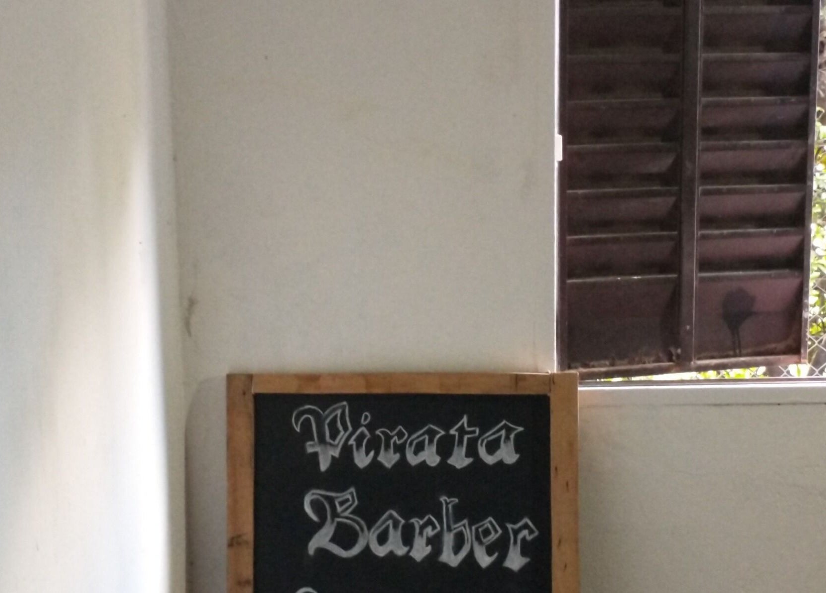 Letrero de Pirataa_Barber en Merlo, San Luis, AR, junto a una ventana abierta con vista al jardín.