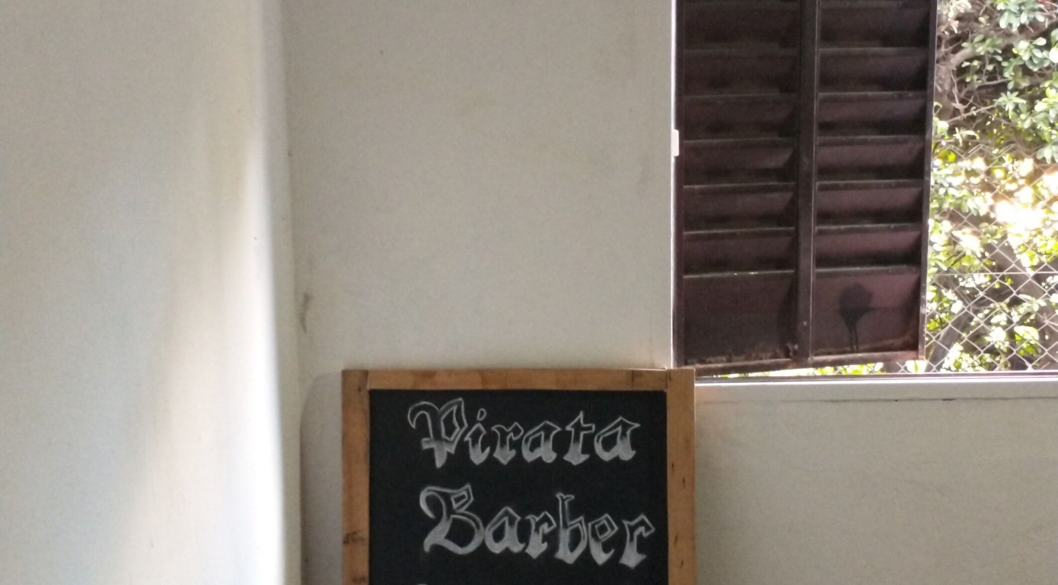 Letrero de Pirataa_Barber en Merlo, San Luis, AR, junto a una ventana abierta con vista al jardín.