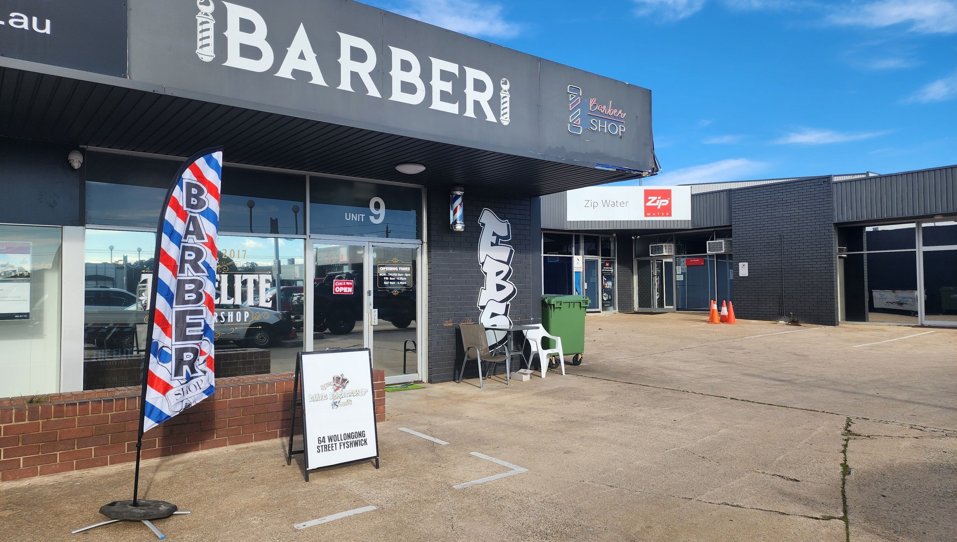 Front view of The Elite Barbershop in Fyshwick, Australian Capital Territory, AU with a vibrant barber pole flag.
