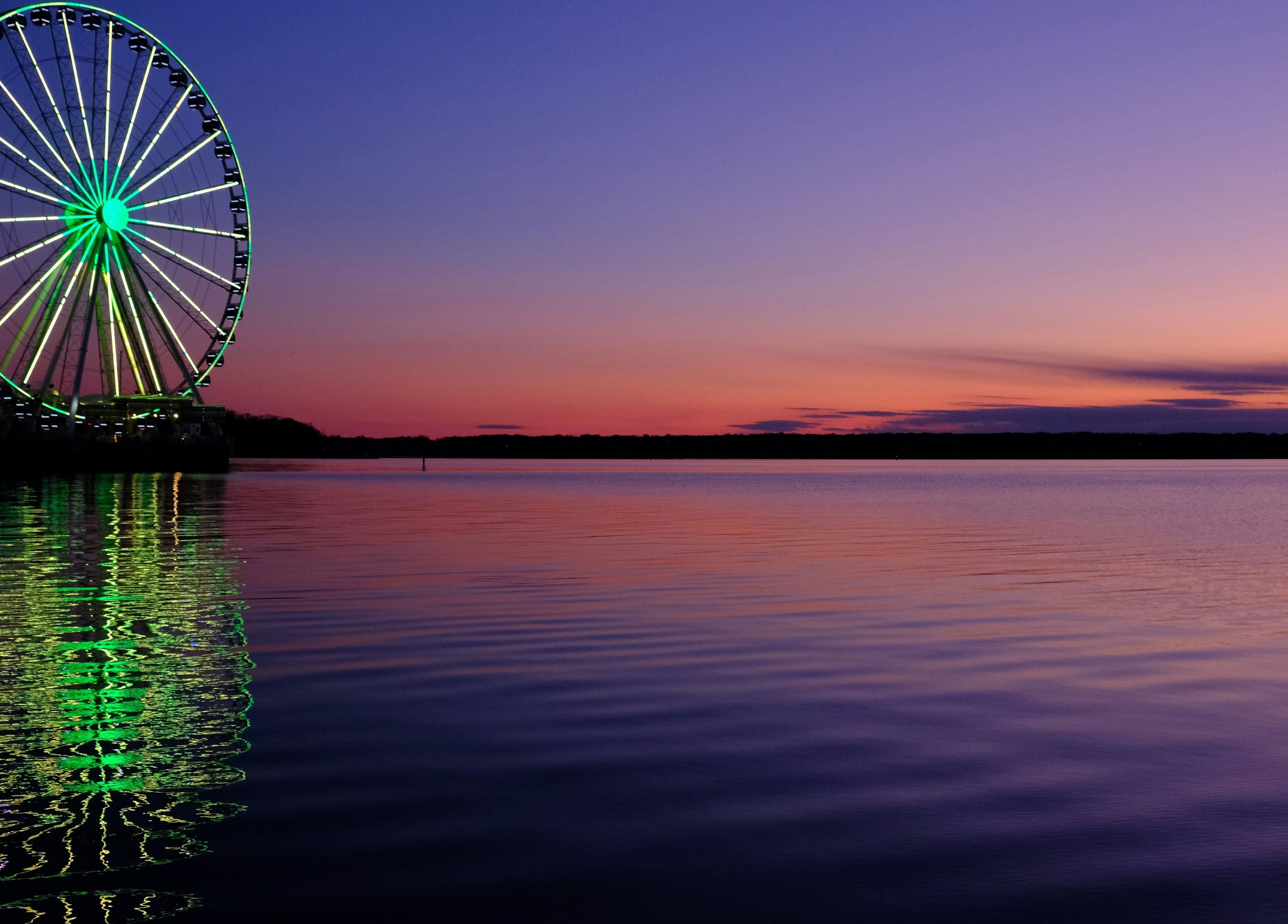 Colorful Ferris wheel reflecting on water at sunset near Le Forbici di Fede, Castello Di Cisterna, Campania, IT.