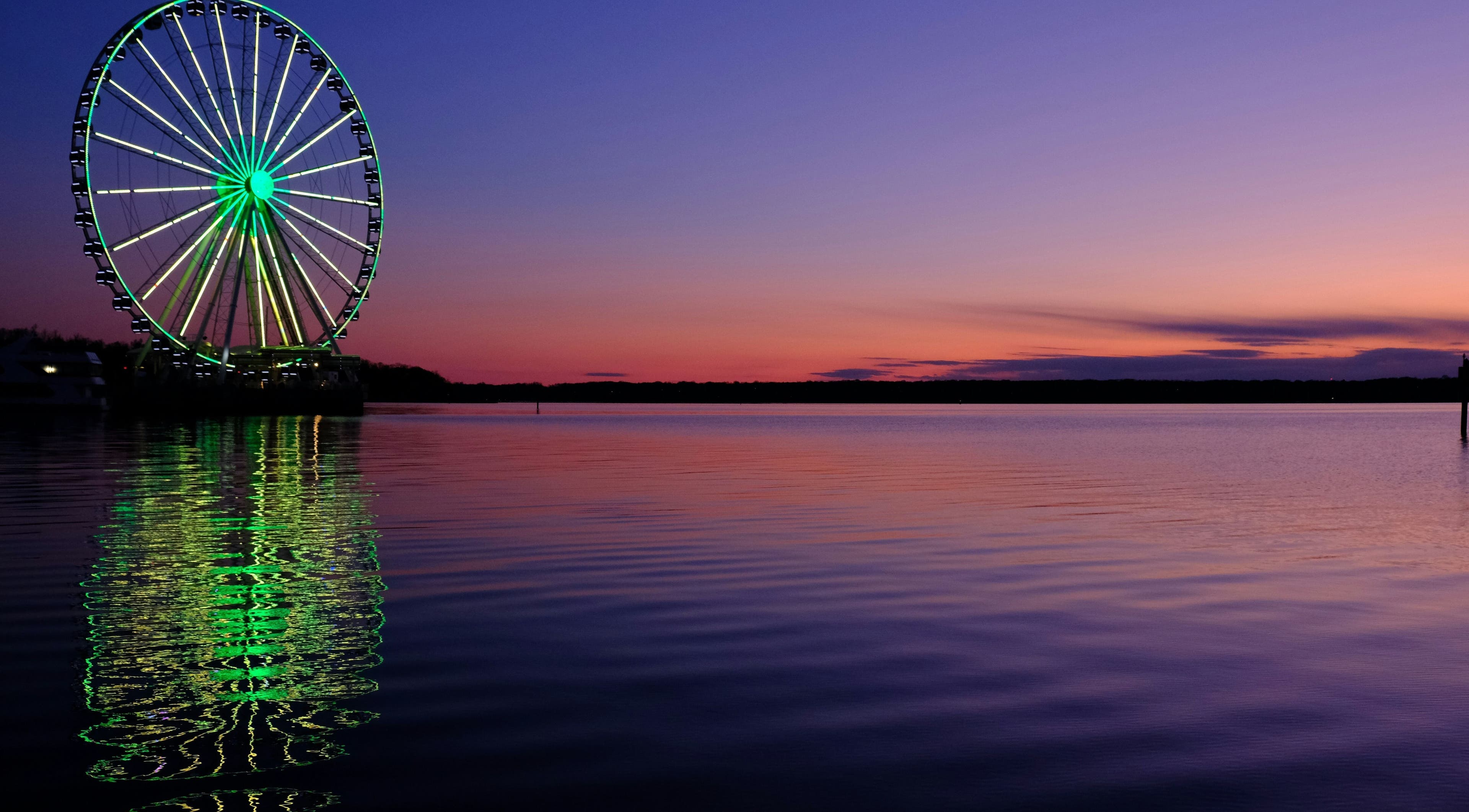 Colorful Ferris wheel reflecting on water at sunset near Le Forbici di Fede, Castello Di Cisterna, Campania, IT.