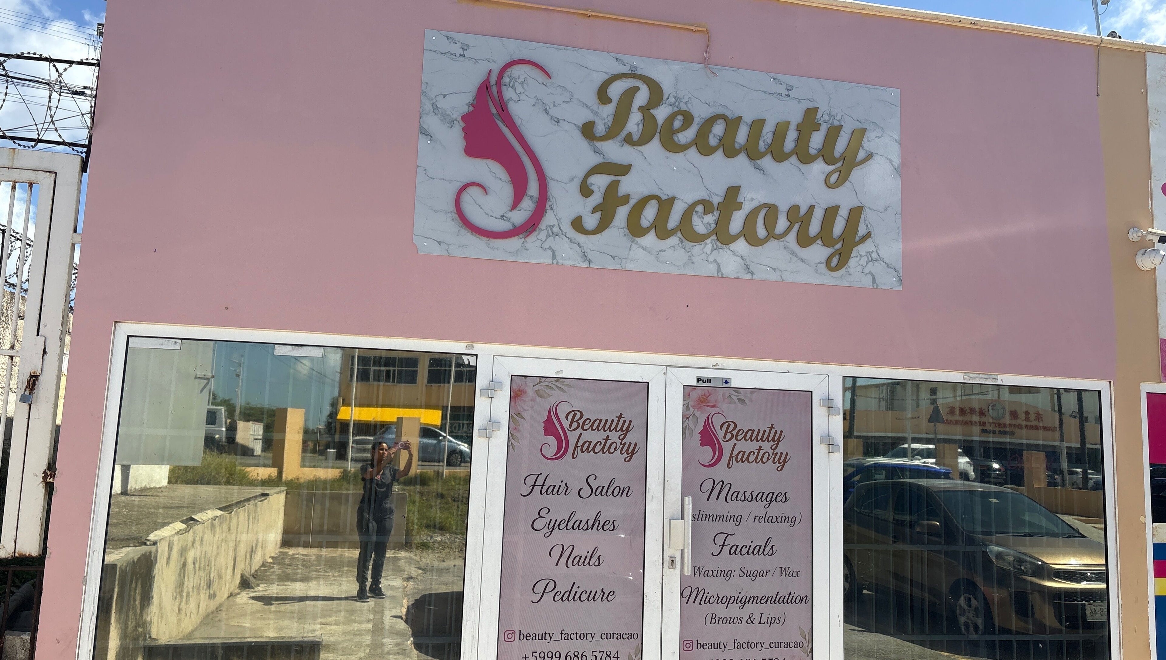 Fachada de Beautyfactorycuracao en Willemstad, Curaçao, CW con cartel rosa y blanco sobre puerta de vidrio.