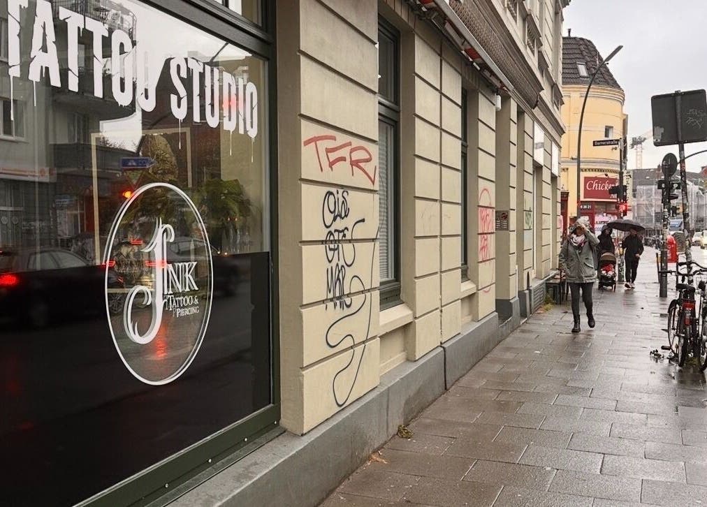 Außenansicht von Schahab Tattoo bei Regen in Hamburg, Hamburg, DE. Passanten und Fahrrad auf der nassen Straße.