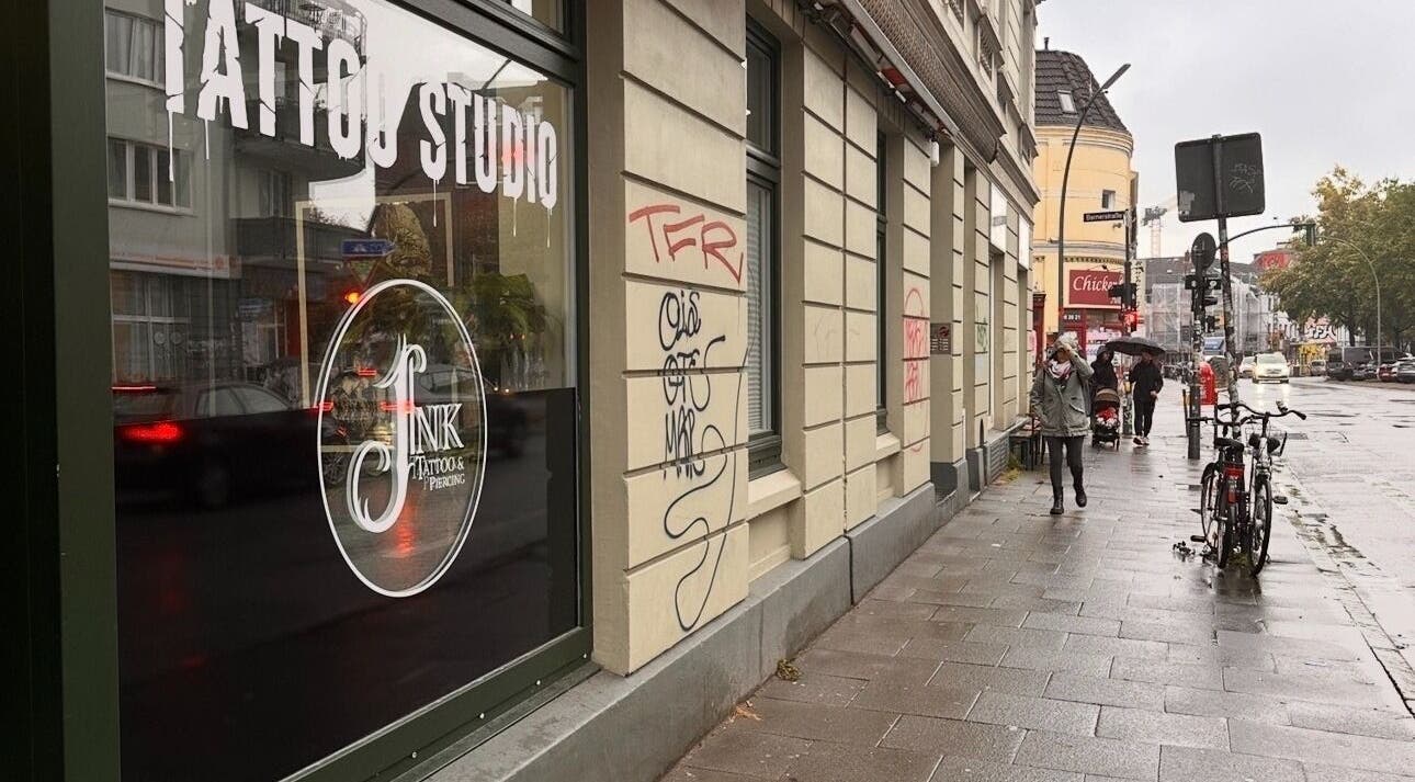 Außenansicht von Schahab Tattoo bei Regen in Hamburg, Hamburg, DE. Passanten und Fahrrad auf der nassen Straße.