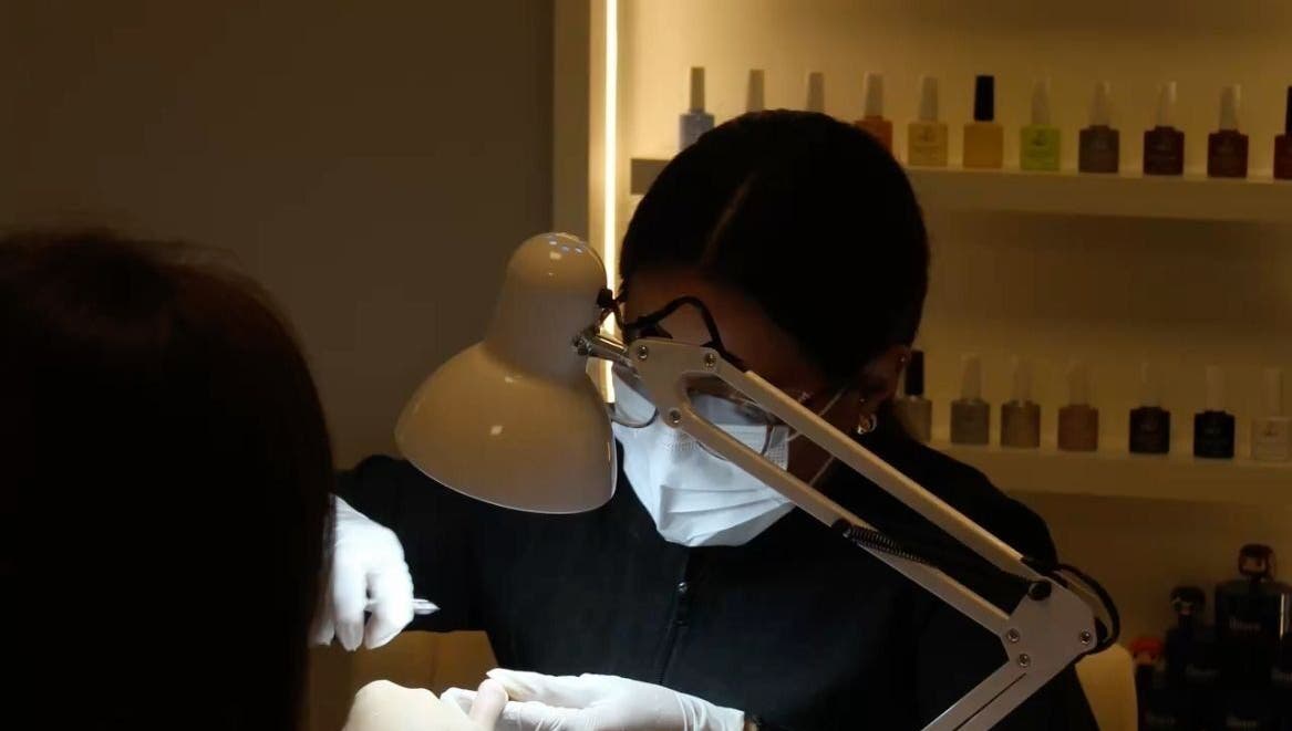 Nail technician at Queen Nails Northfield Spa in Birmingham, England, GB, providing manicure service under a lamp.