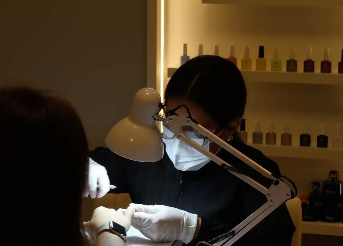Nail technician at Queen Nails Northfield Spa in Birmingham, England, GB, providing manicure service under a lamp.