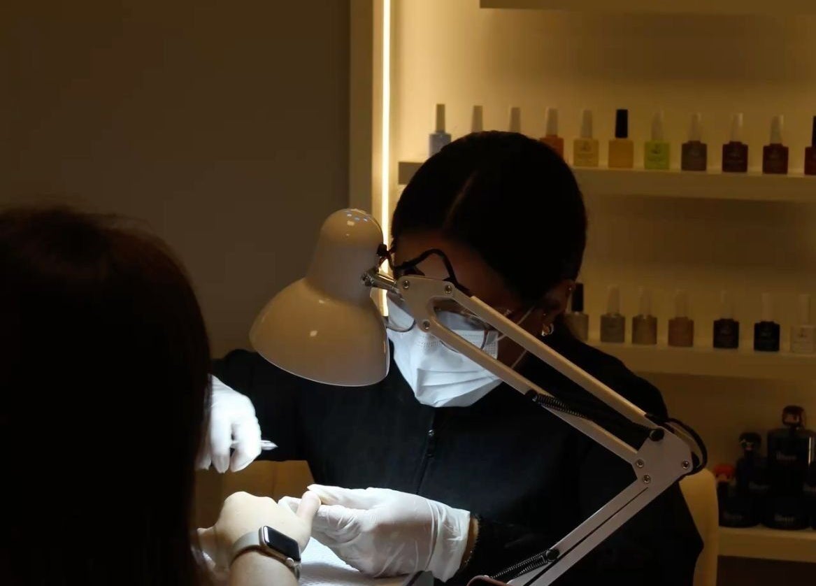 Nail technician at Queen Nails Northfield Spa in Birmingham, England, GB, providing manicure service under a lamp.