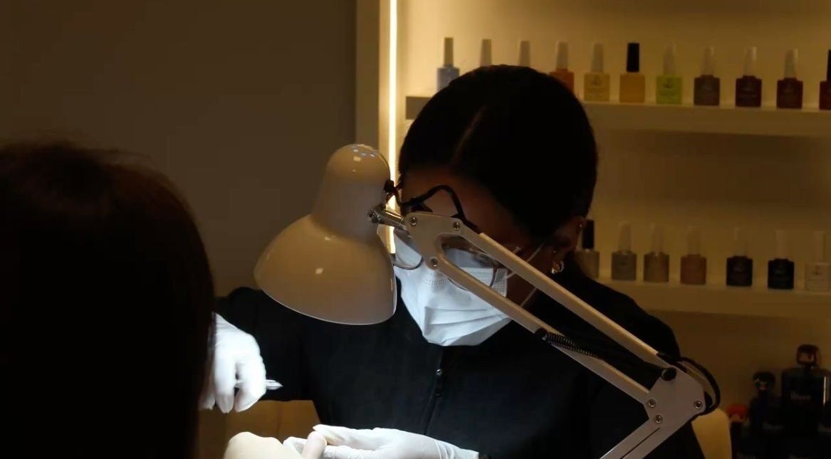 Nail technician at Queen Nails Northfield Spa in Birmingham, England, GB, providing manicure service under a lamp.