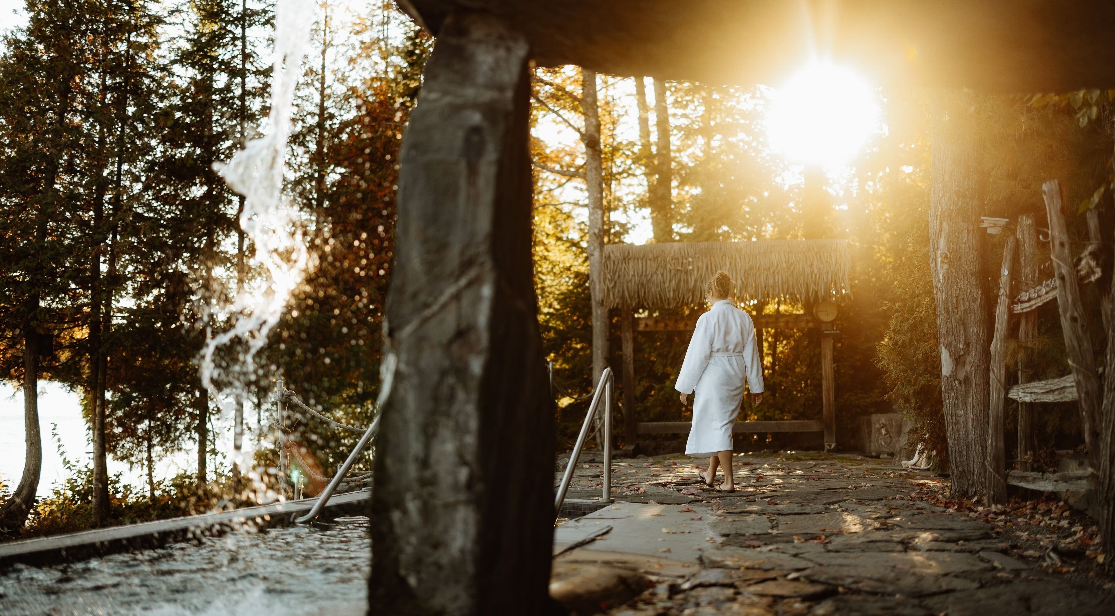 Femme en peignoir à Sartiga Spa sur le Lac, Saint-alfred, Québec, CA, entourée de nature et cascades.