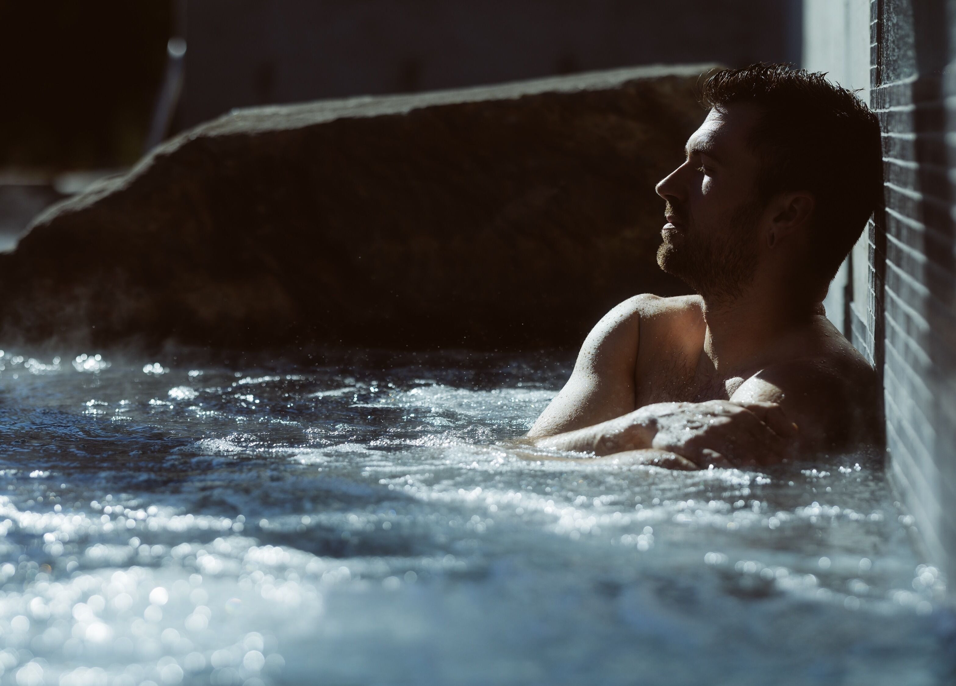 Homme relaxant au Sartiga Spa sur le Lac, Saint-alfred, Québec, CA, dans un bain extérieur ensoleillé.