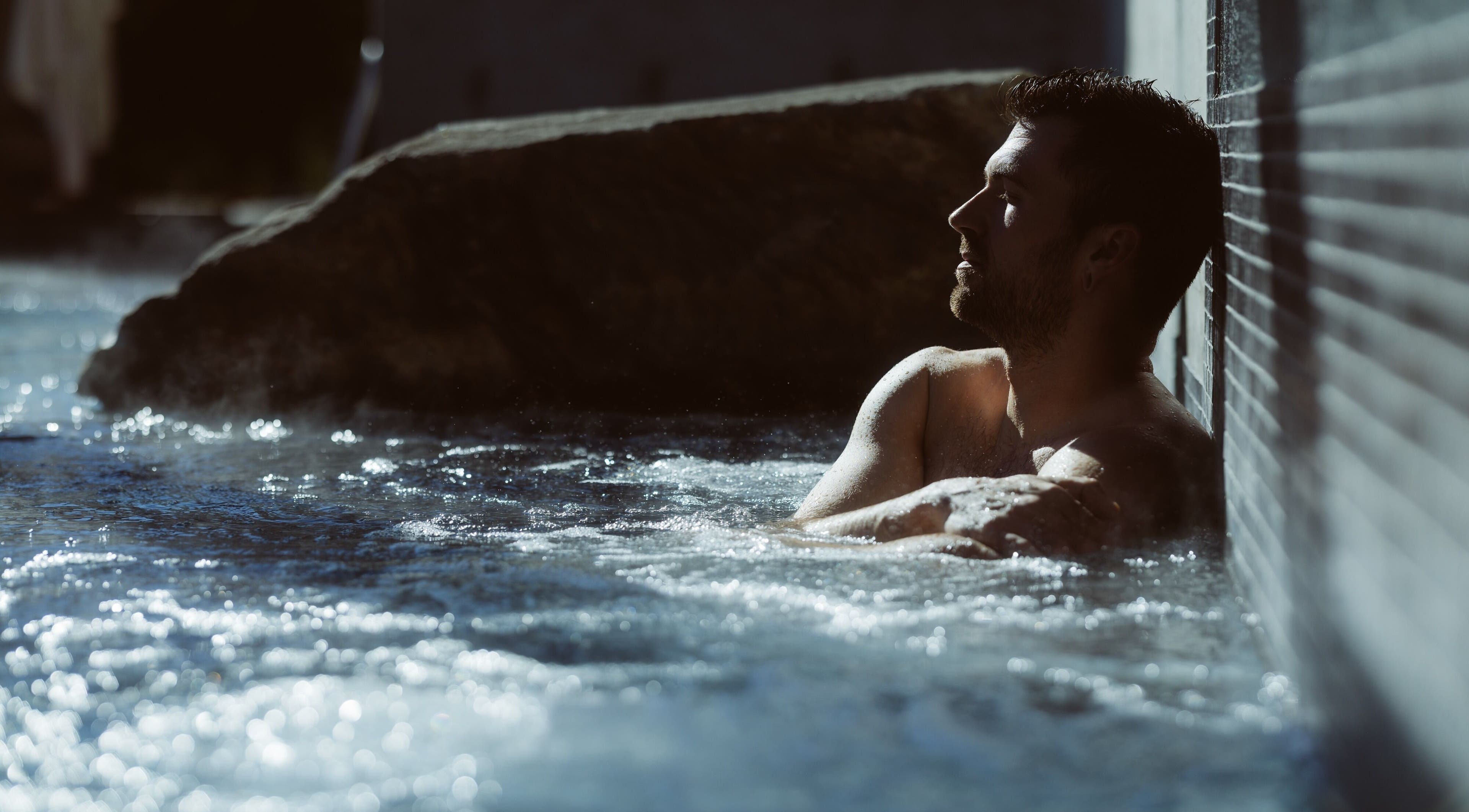 Homme relaxant au Sartiga Spa sur le Lac, Saint-alfred, Québec, CA, dans un bain extérieur ensoleillé.