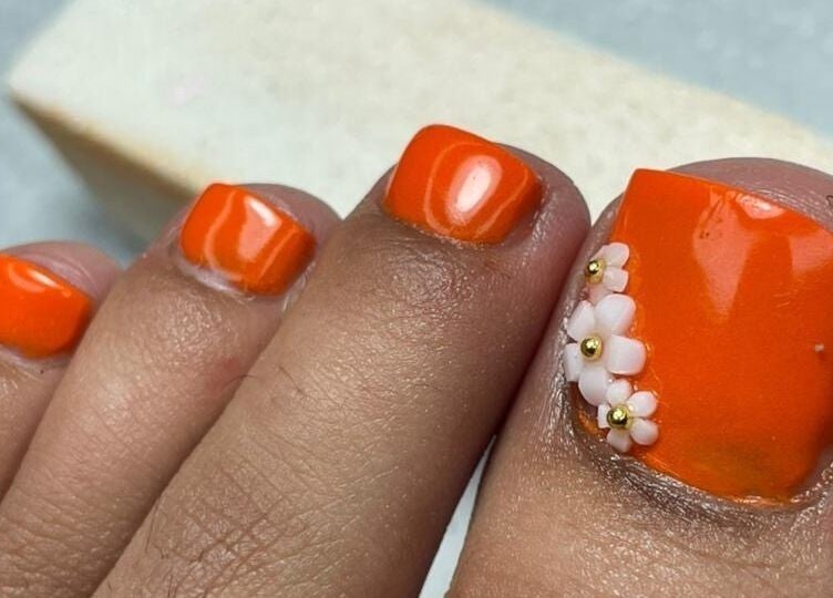 Bold orange pedicure with floral accents at UR HONESTY BEAUTY CO. STUDIO, Roodepoort, Gauteng, ZA.
