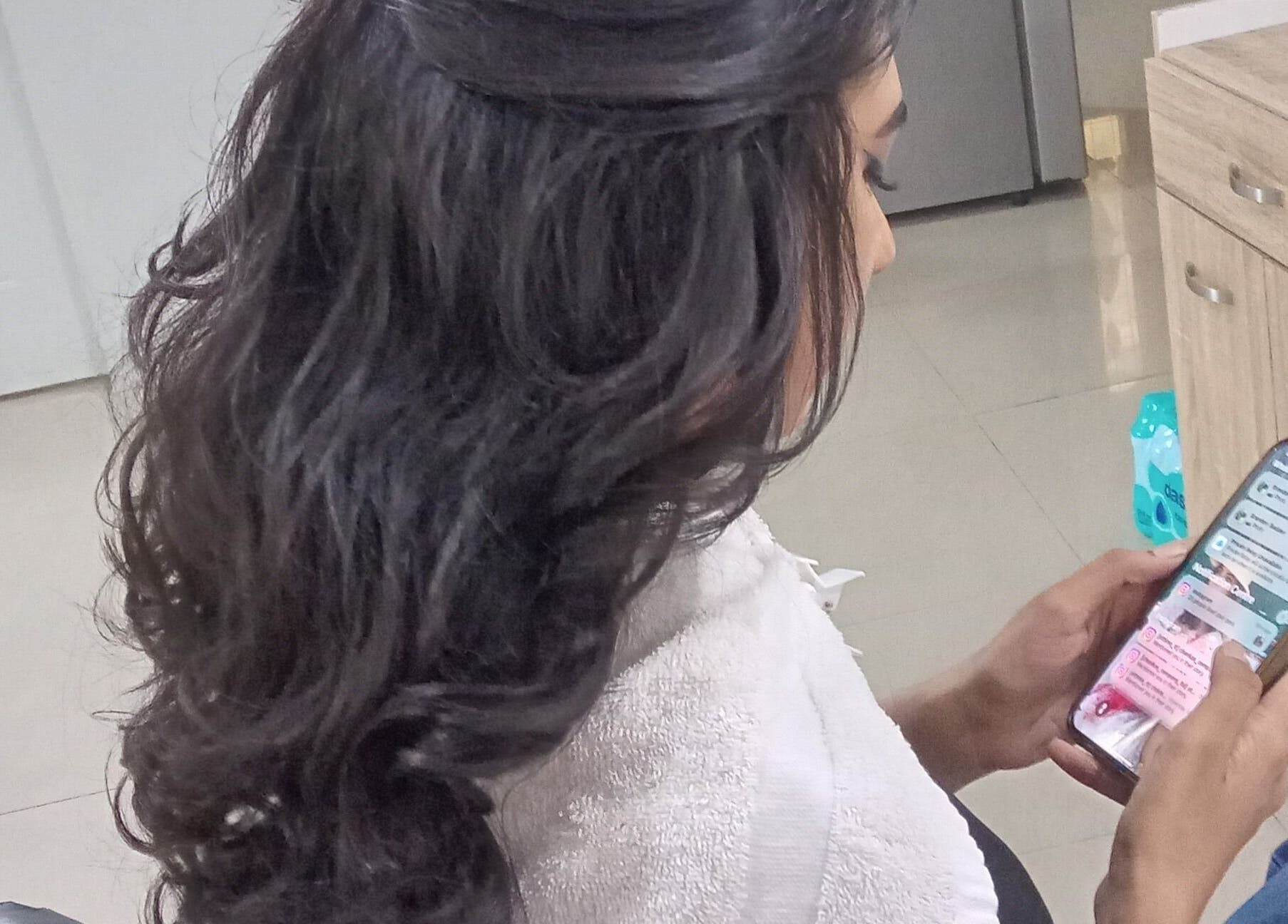 Client with styled hair browsing phone at R. Luxe Hair Studio, Chaguanas, Chaguanas, TT.