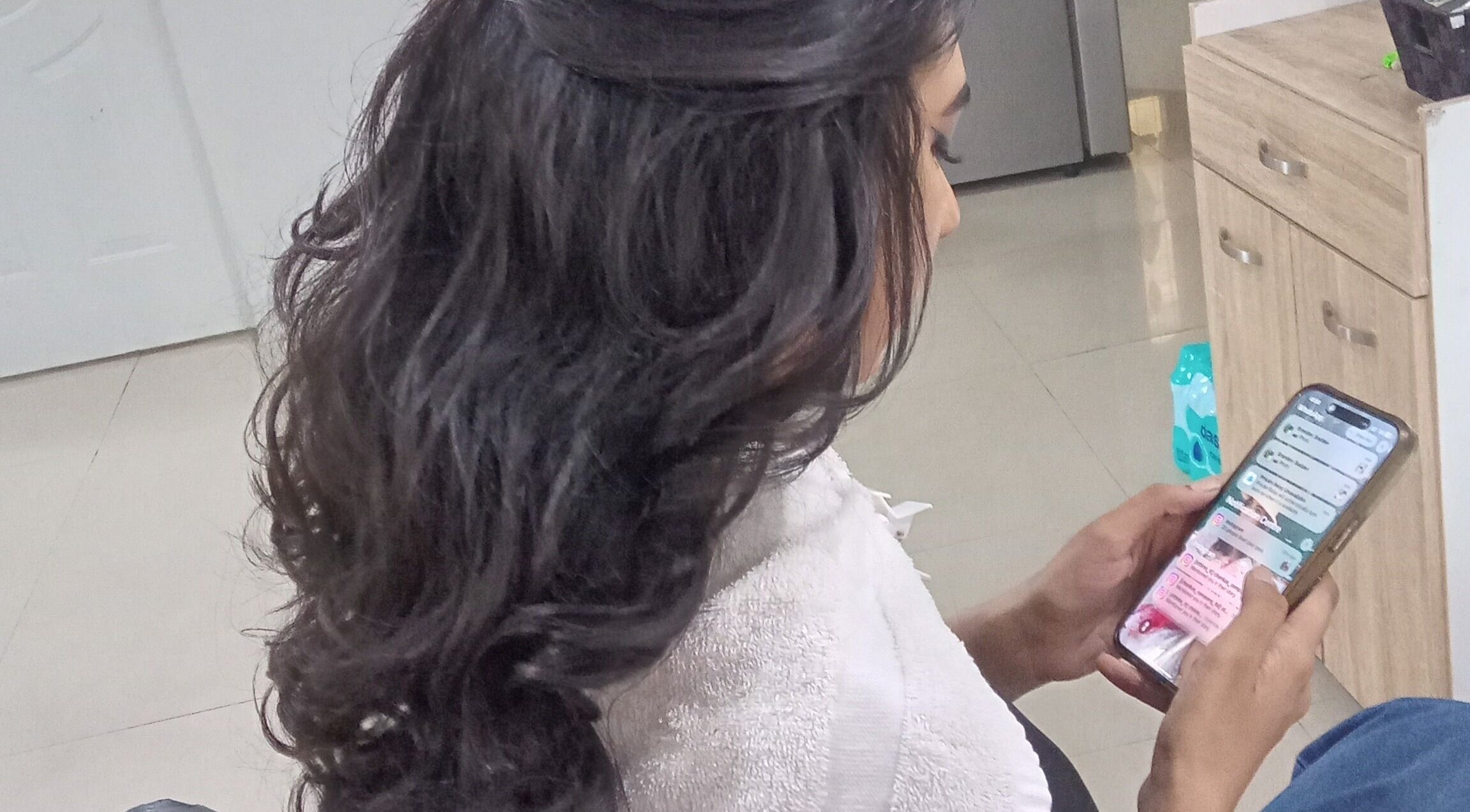 Client with styled hair browsing phone at R. Luxe Hair Studio, Chaguanas, Chaguanas, TT.