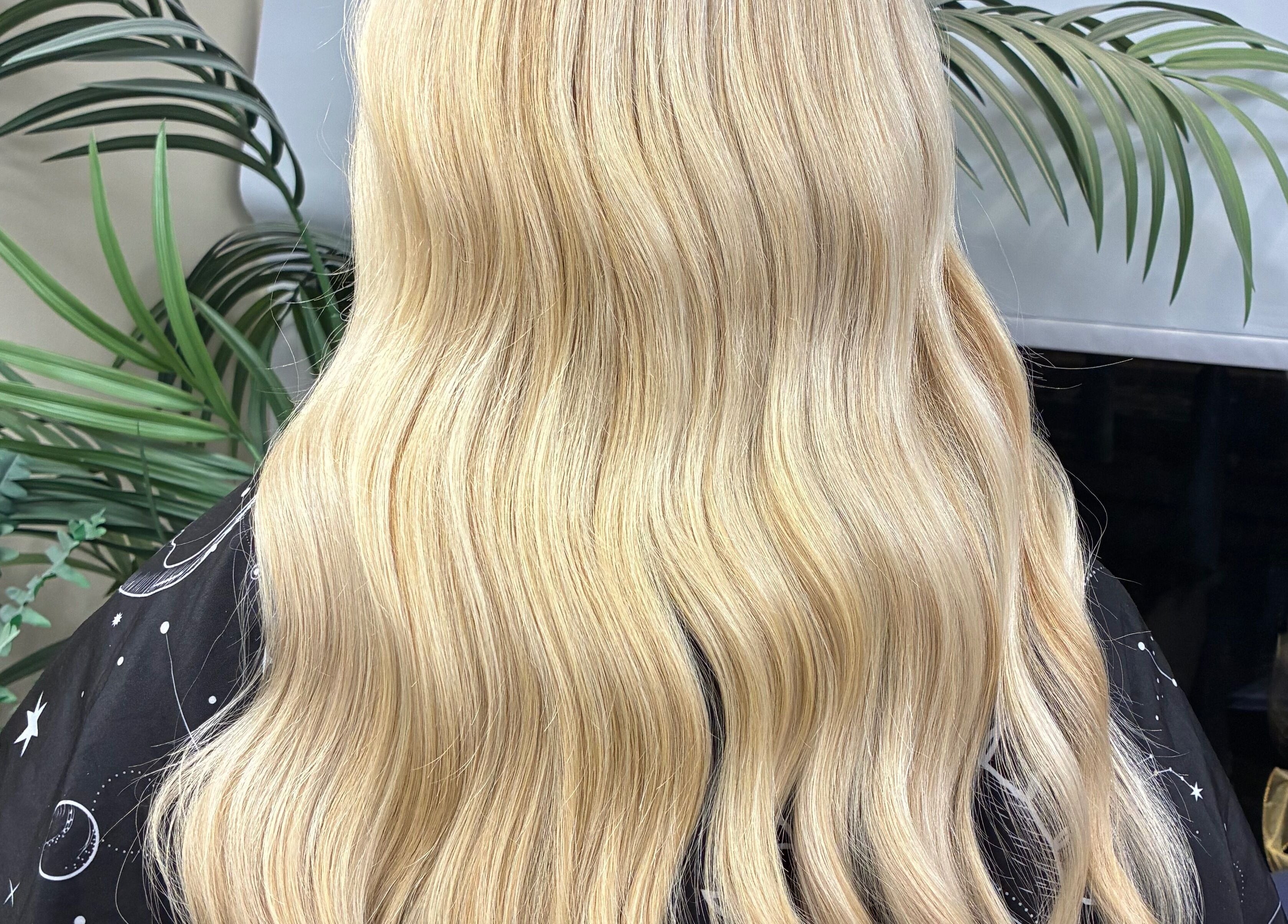 Long blonde waves styled at Navie Studio, Hull, England, GB, framed by lush green plants.