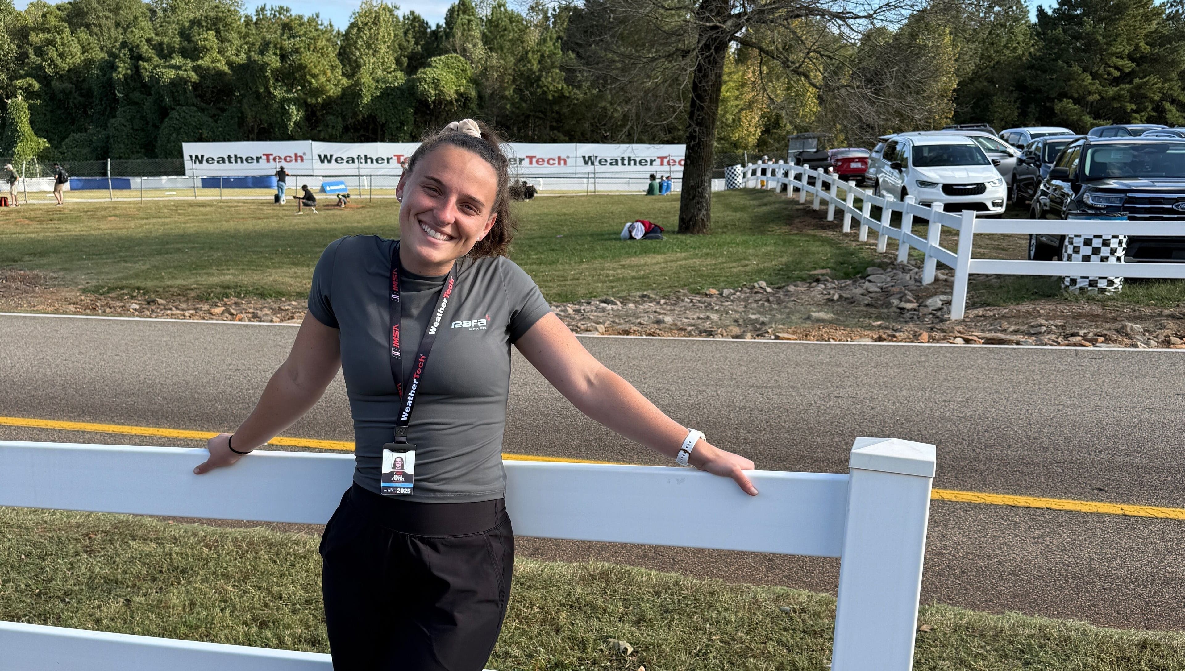 Woman smiling by fence at Strides Performance in Stamford, Connecticut, US, under blue sky.