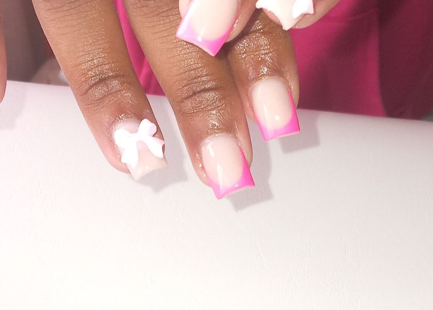 Vibrant pink nail art with white bow at ZEE.NAILS, Sebokeng, Gauteng, ZA, showcasing creative designs.
