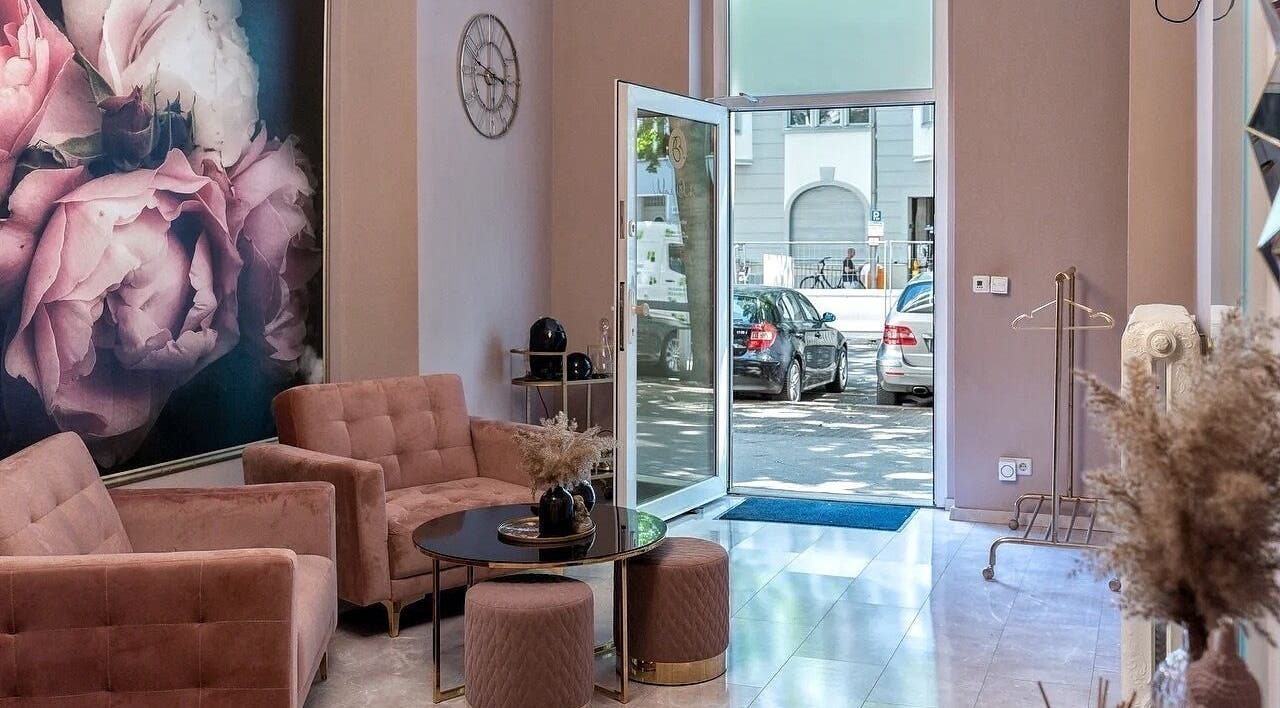 Элегантный интерьер Massage by Ella (Massage nur Frauen) в Берлине, DE с розовыми диванами и цветочной живописью.