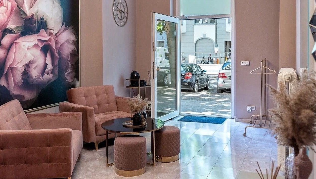 Элегантный холл в Massage by Ella (Massage nur Frauen), Берлин, Германия с розовыми диванами и настенной росписью.