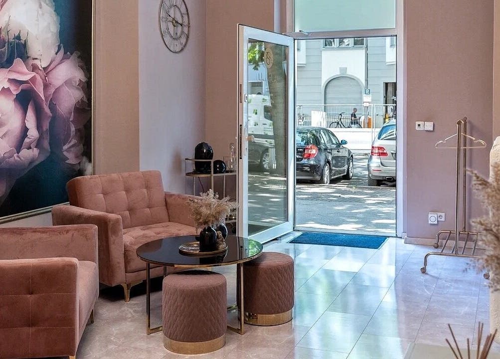 Элегантный холл в Massage by Ella (Massage nur Frauen), Берлин, Германия с розовыми диванами и настенной росписью.