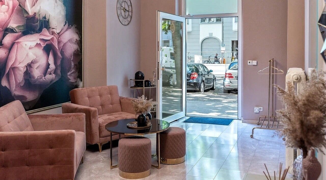 Элегантный холл в Massage by Ella (Massage nur Frauen), Берлин, Германия с розовыми диванами и настенной росписью.