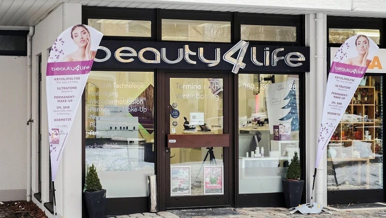 Eingang von Beauty4Life in München, Bayern, DE, mit Werbeschildern und moderner Glasfassade.