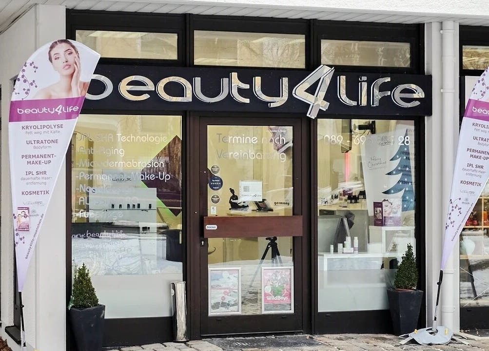 Eingang von Beauty4Life in München, Bayern, DE, mit Werbeschildern und moderner Glasfassade.
