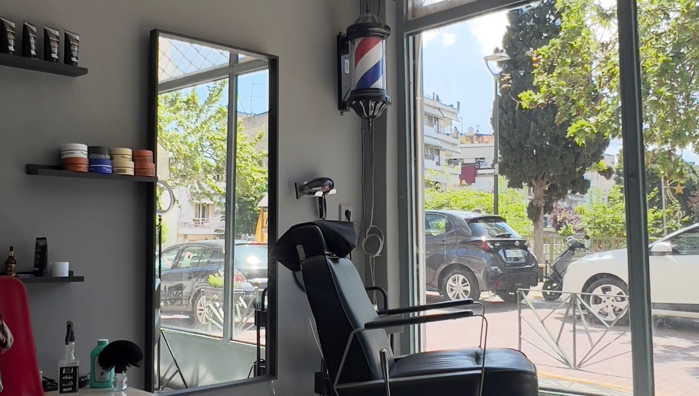 Inside NALDO HAIR STUDIO Neapoli, GR with chair and street view through large windows.