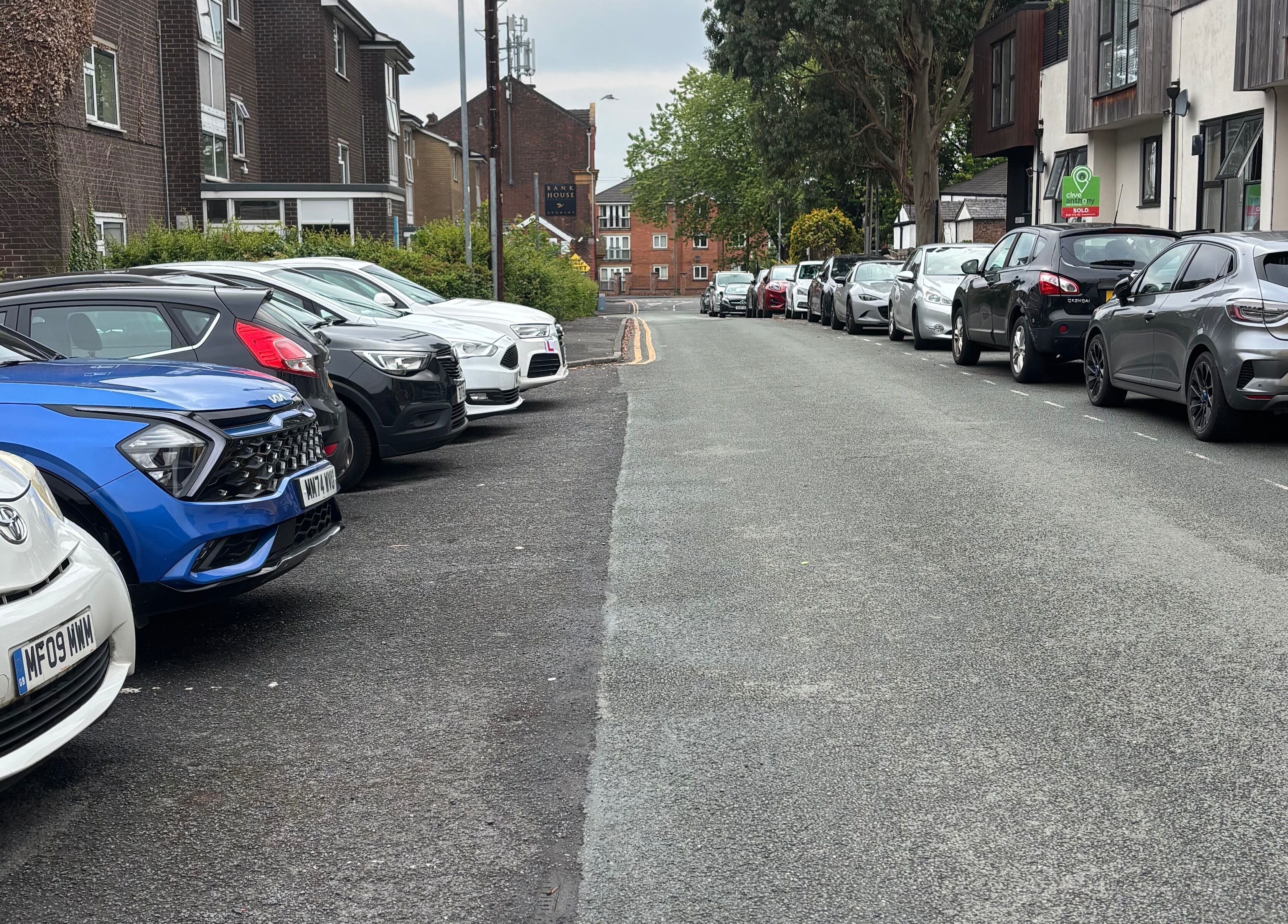 Street view near Ej beauty service, Prestwich, England, GB with parked cars aligning the roadway.