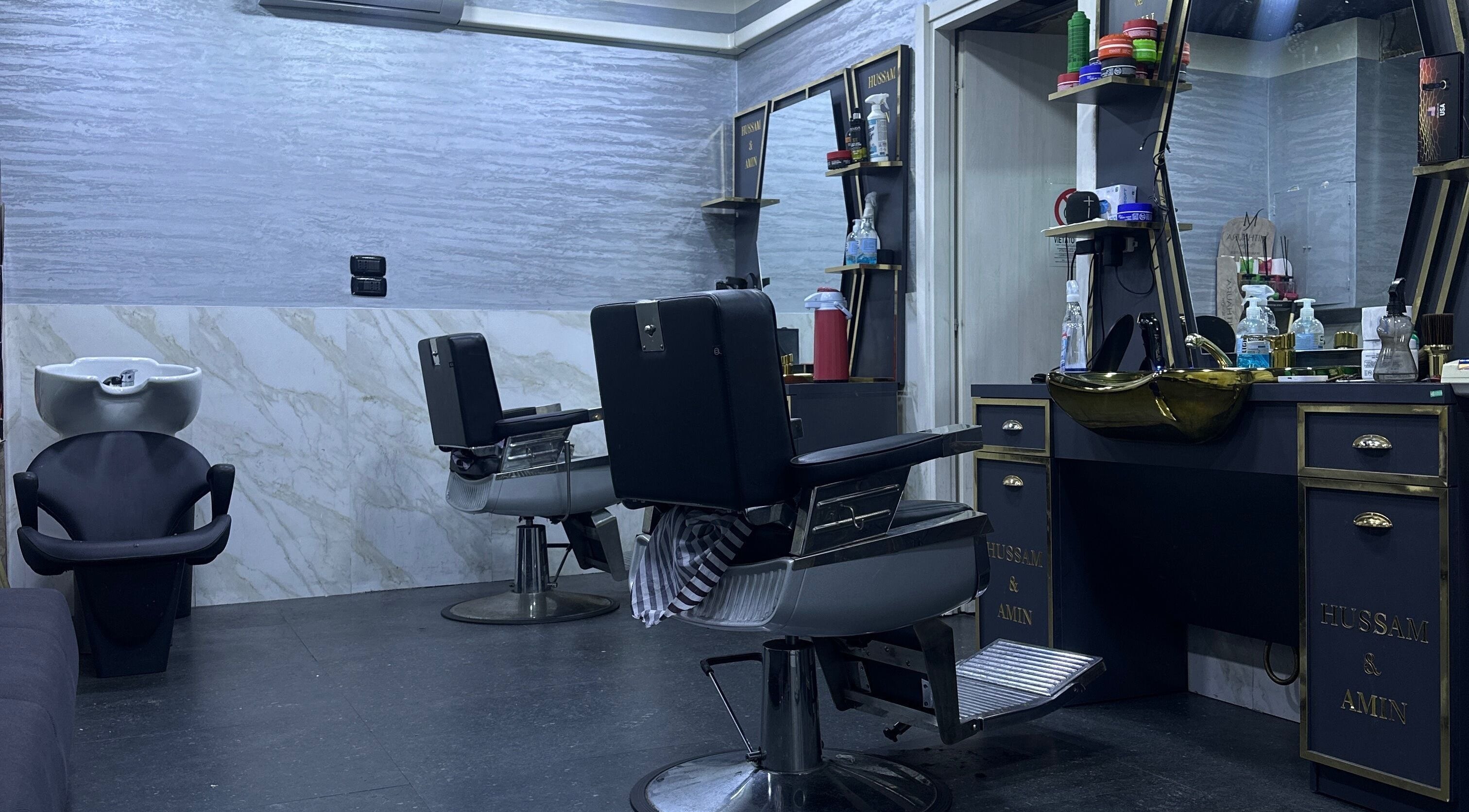 Sala moderna di BARBER HOSSY a Genova, Liguria, IT, con poltrone nere e lavandino elegante.