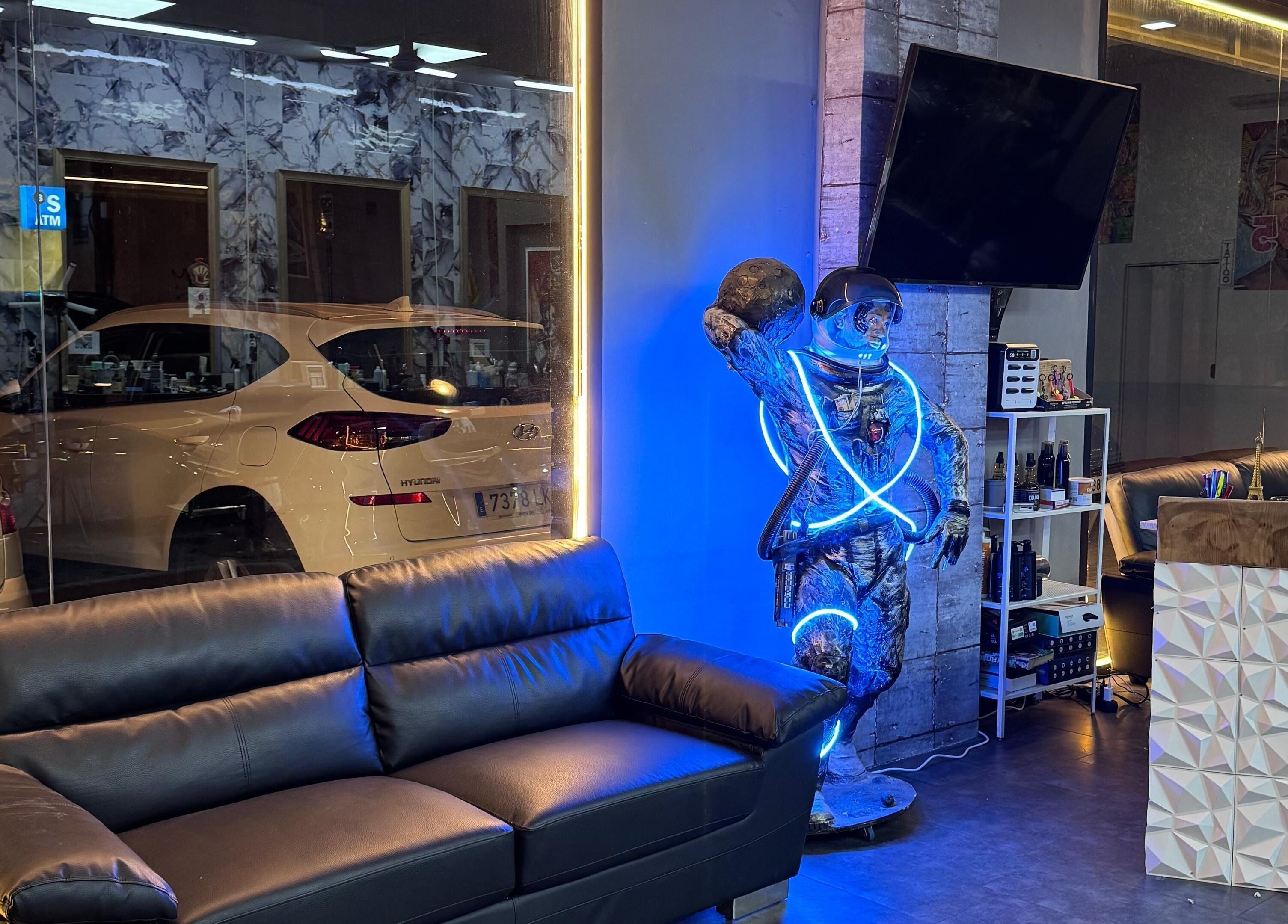 Interior de 305 Barberia en València con sofá negro y astronauta iluminado en neón azul.