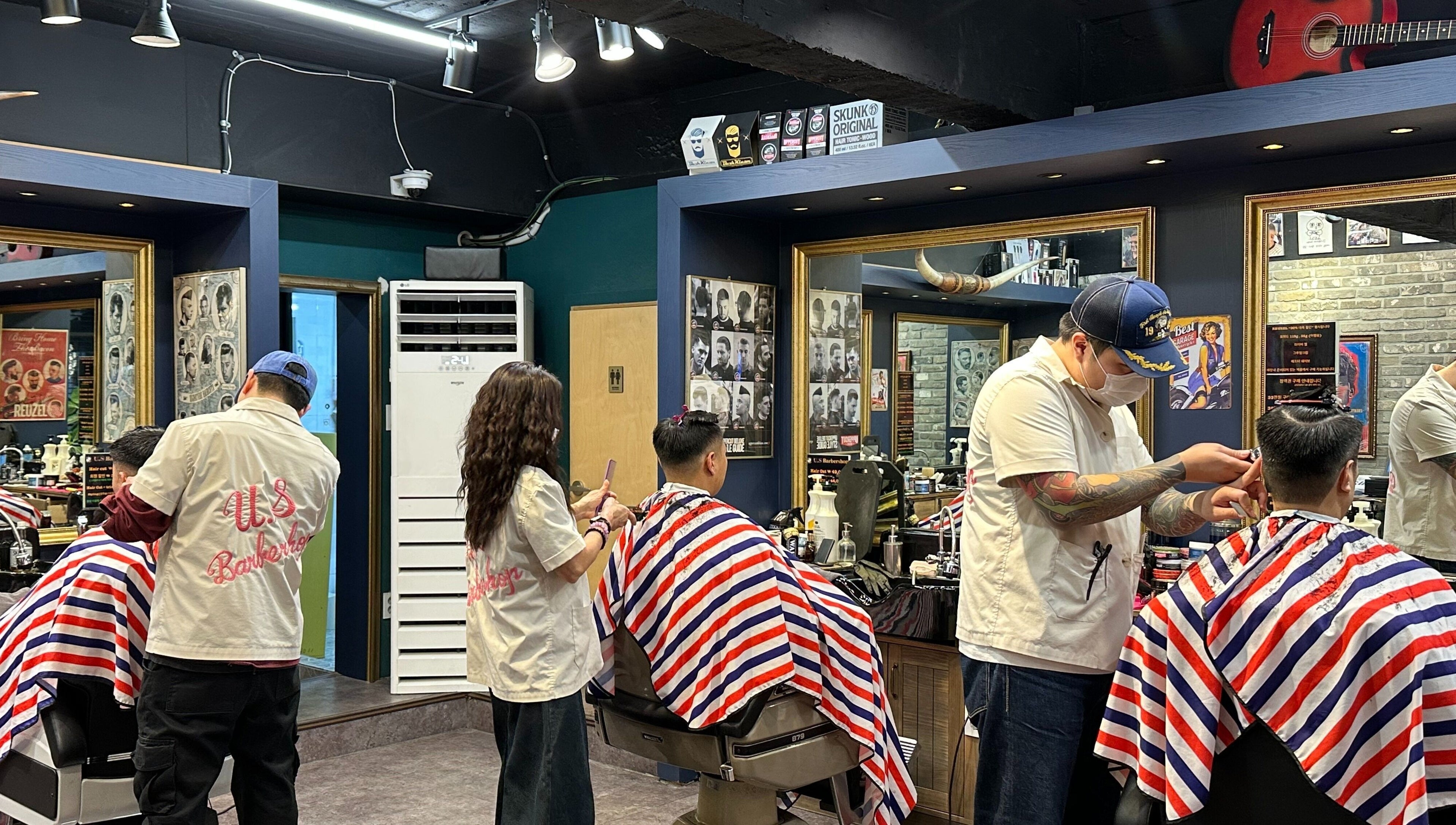 Stylists at US Barbershop, 서울특별시, KR, trim hair under modern lighting with red-white-blue capes.