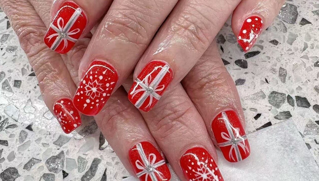 Red festive nail designs at YOYO NAILS, Noblesville, Indiana, US showcase intricate white patterns.