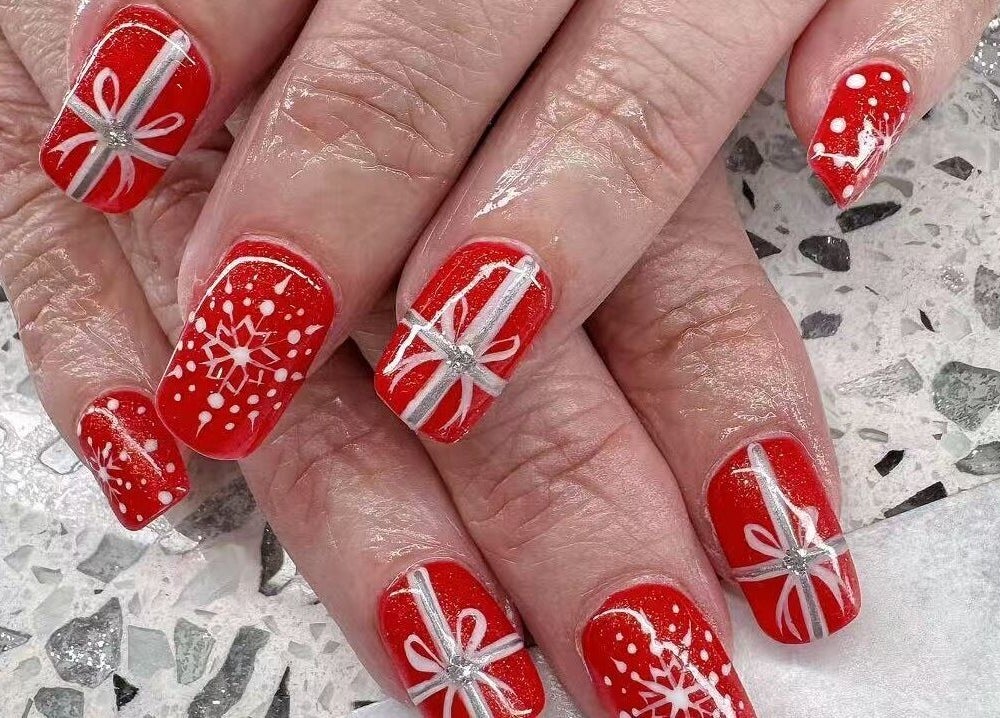 Red festive nail designs at YOYO NAILS, Noblesville, Indiana, US showcase intricate white patterns.