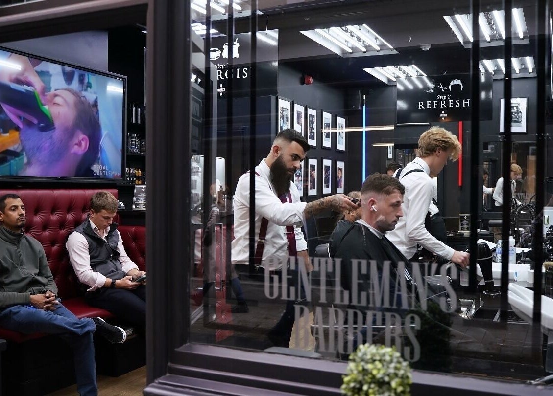 Stylish barbershop interior at Bar Bar Co, Brentwood, England, GB with clients relaxing and getting haircuts.