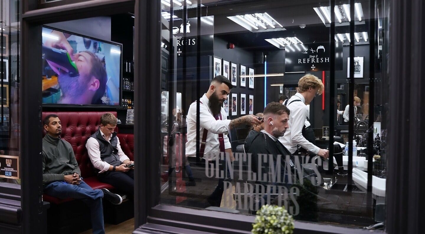 Stylish barbershop interior at Bar Bar Co, Brentwood, England, GB with clients relaxing and getting haircuts.
