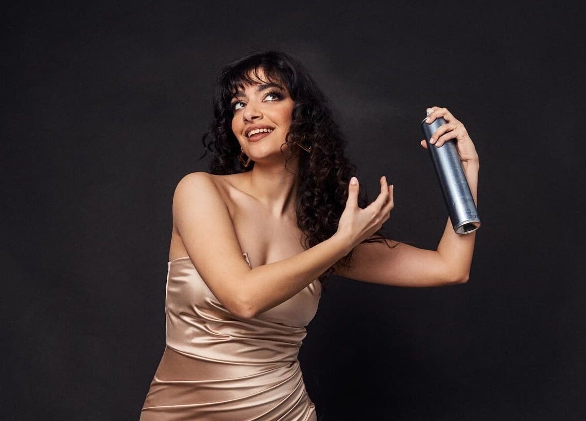 Γυναίκα σε σατέν φόρεμα εφαρμόζει σπρέι μαλλιών στο Panos Vivendo Creative Hair Design, Λεμεσός, Λεμεσός, CY.