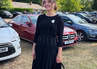Smiling person standing stylishly beside cars in London, showcasing beauty by B Yo Uty Hair and Beauty Mobile Service.