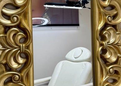 Elegant gold-framed mirror at Trends Aesthetic Beauty Salon, London, England, GB next to a white treatment chair.