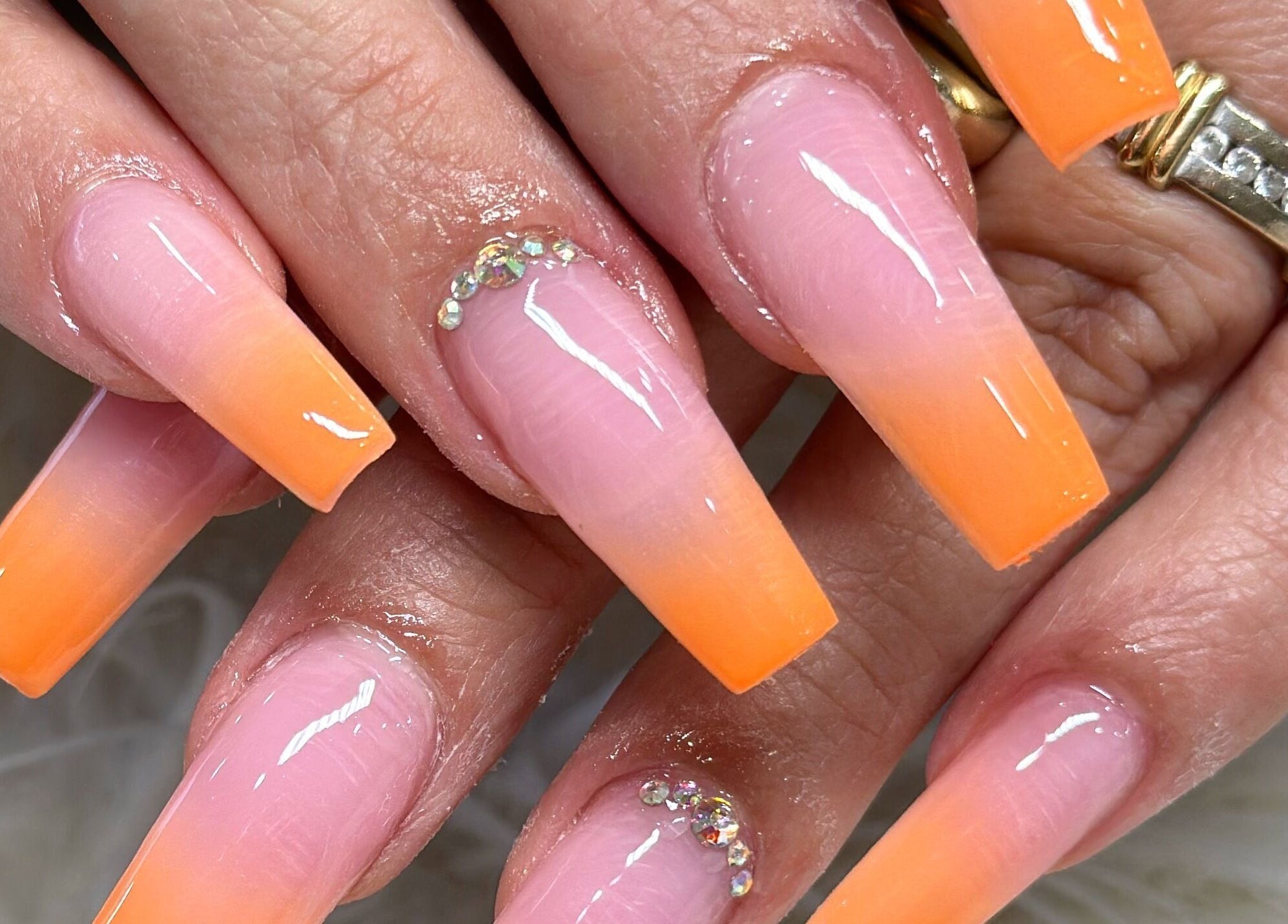 Elegant ombre nails in orange and pink with rhinestones at Glamor Nails, Bound Brook, New Jersey, US.