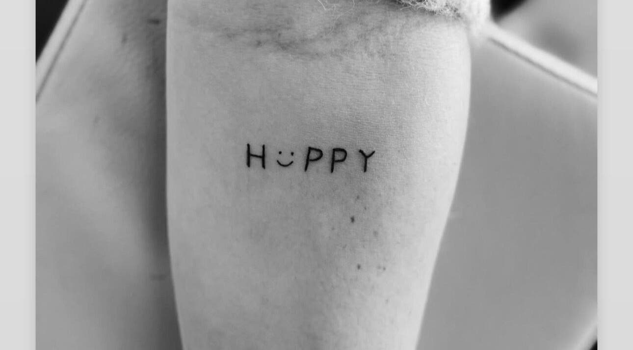 Minimalist 'Happy' tattoo at The Lash Bar, Holland-on-sea, England, GB showcasing unique artistic style.