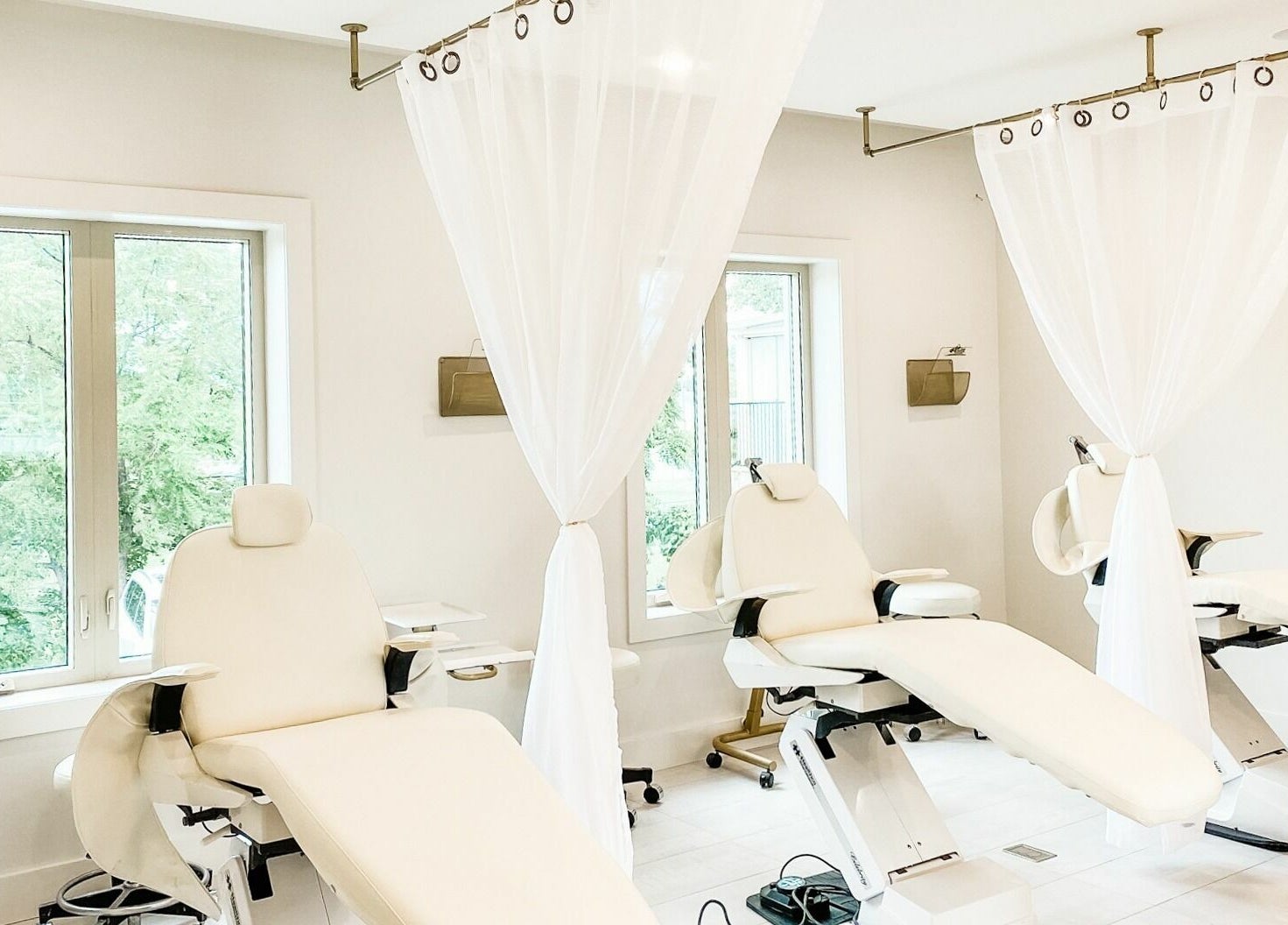Bright treatment room at Elixir Beauty Mixology, Niagara Falls, Ontario, CA with white reclining chairs and sheer curtains.