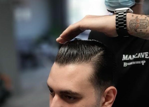 Barber styling hair at Mancave Barbershop, Limassol, Limassol, CY. Tattooed arm with watch visible.