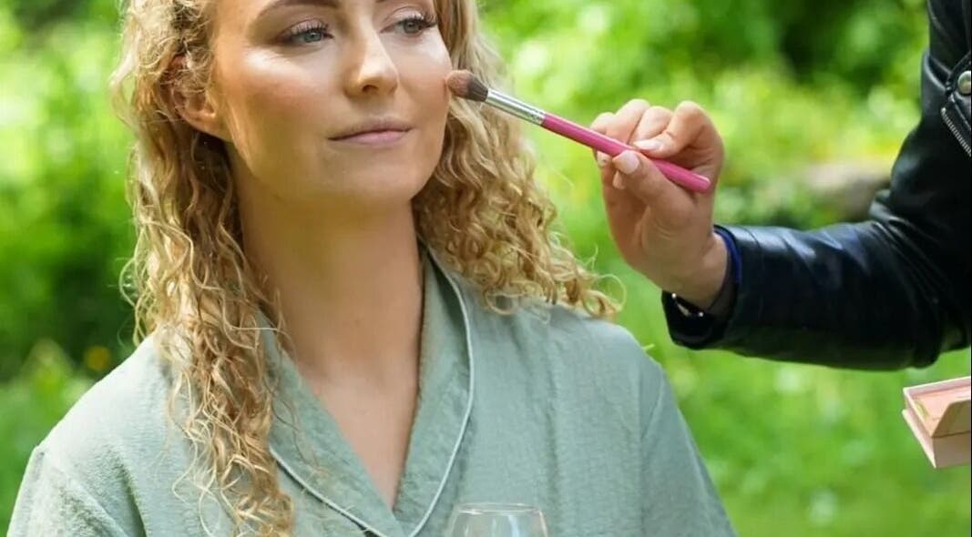 Makeup artist applies blush at Kerie Beauty, Saint Asaph, Wales, GB, enhancing a woman's complexion outdoors.