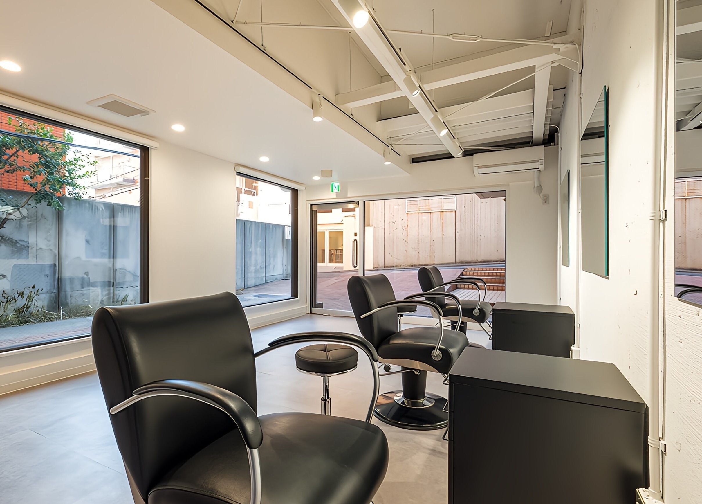 Chic interior of FÈATH salon in Minato City, Tokyo, JP, featuring sleek black chairs and large windows.