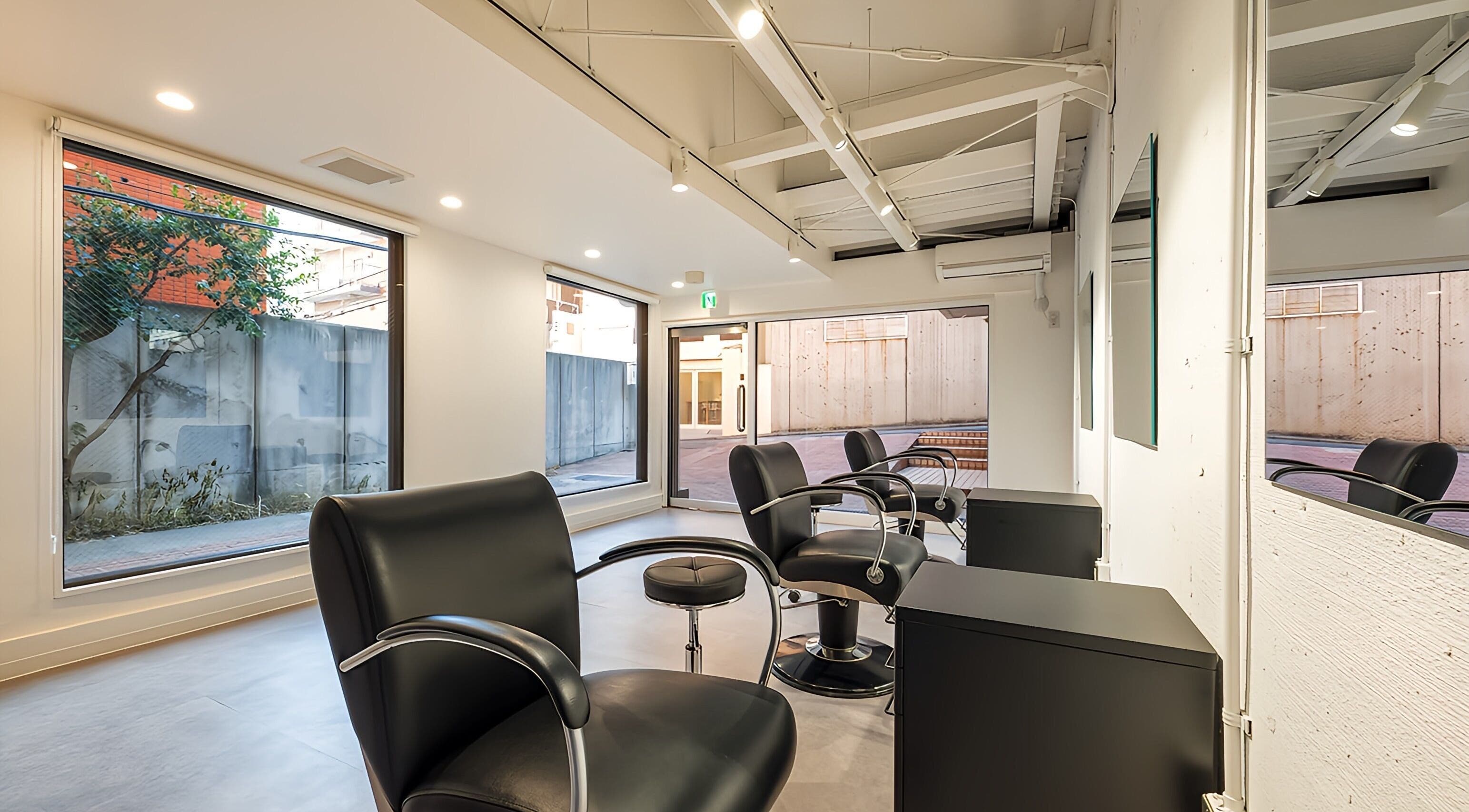 Chic interior of FÈATH salon in Minato City, Tokyo, JP, featuring sleek black chairs and large windows.