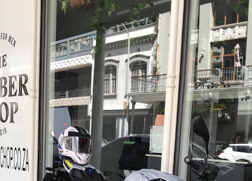 Front view of The Barberchop in Cape Town, Western Cape, ZA, showcasing window signage with helmets outside.