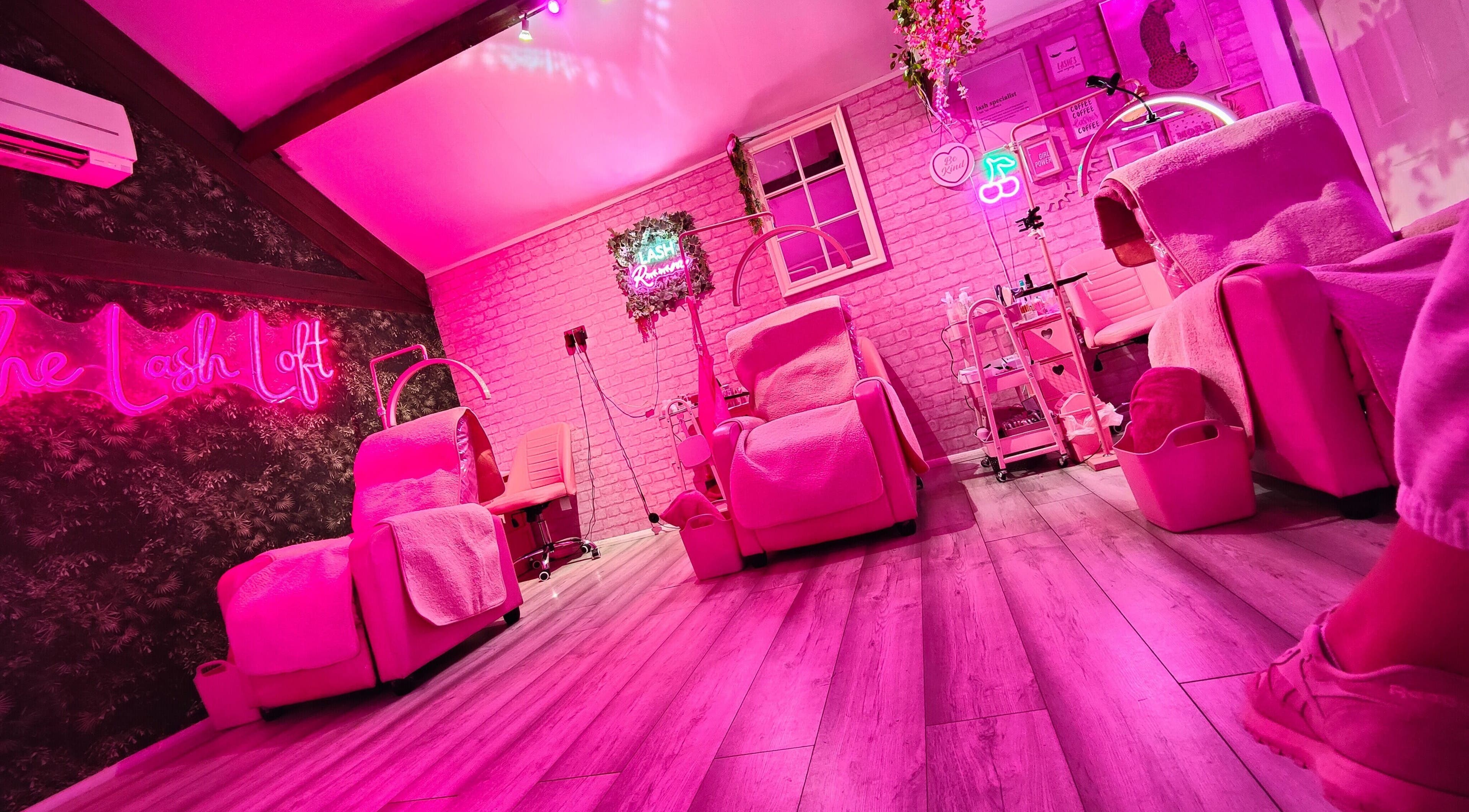 Relaxing pink-lit interior of The Lash Loft in Scarborough, England, GB showcasing luxury chairs and neon signs.