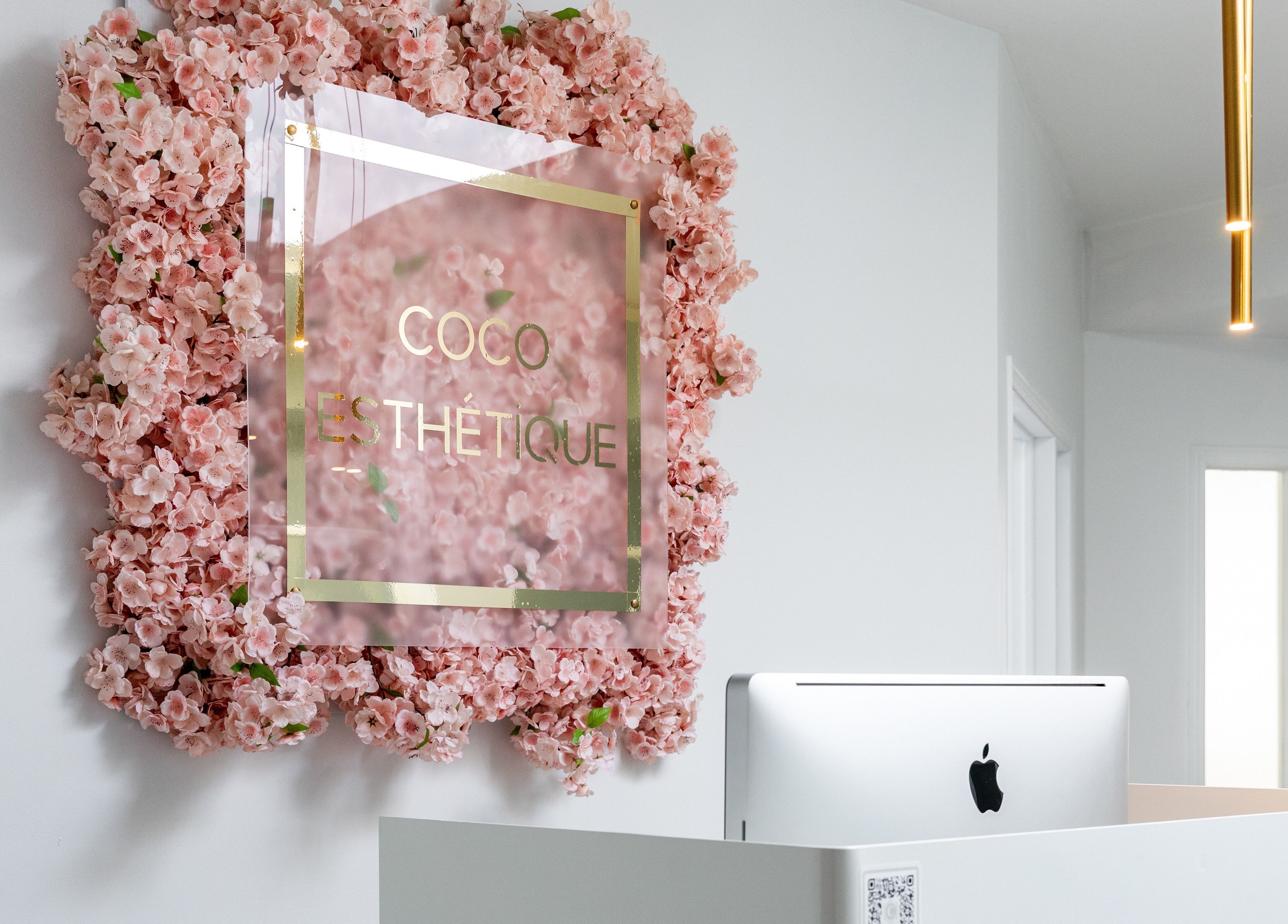 Entrée florale Chez Coco Esthétique, Montréal, Québec, CA avec des fleurs roses autour de l'enseigne.